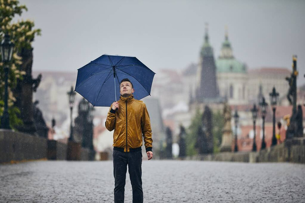 Lonely man with umbrella in heavy rain on empty Charles Bridge. Prague Czech Republic - Photo, Image