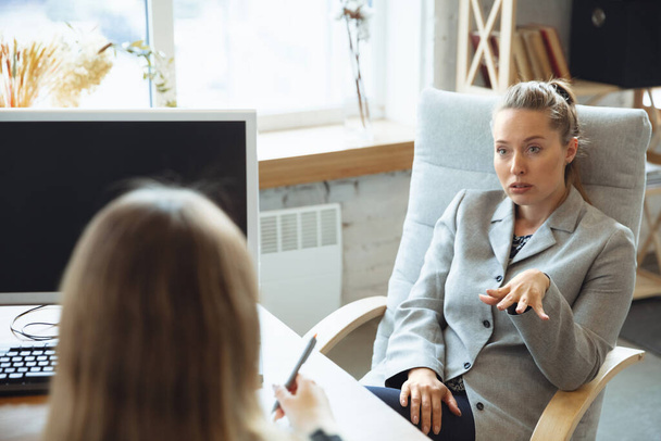 Young woman in suit sitting in office during the job interview with female employee, boss or HR-manager, talking, thinking, looks confident - Foto, immagini