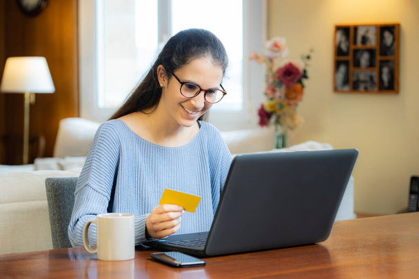 Szczęśliwa młoda dziewczyna z okularami zakupy online z laptopem z domu - Zdjęcie, obraz