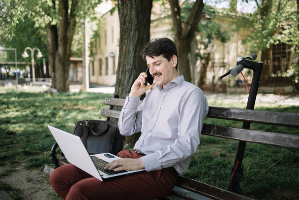 Vista lateral del hombre sonriente con portátil hablando por teléfono
 - Foto, Imagen