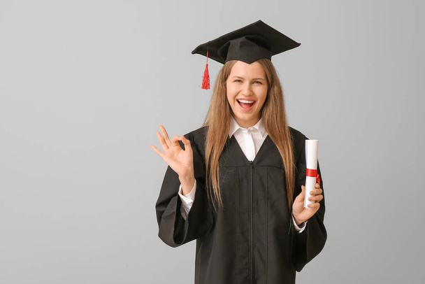Female graduating student with diploma showing OK on light background - Photo, Image