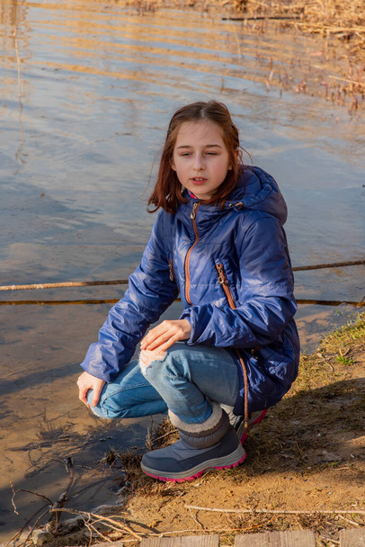 Açık renk koyun derisi ceketli bir kız güneşli bir günde nehrin kıyısında duruyor. 9 yaşında, nehir kıyısında koyun derisi ceketli bir kız. Kız 9 yaşında ya da 10 yaşında. Doğa, çocuk, liseli kız. - Fotoğraf, Görsel