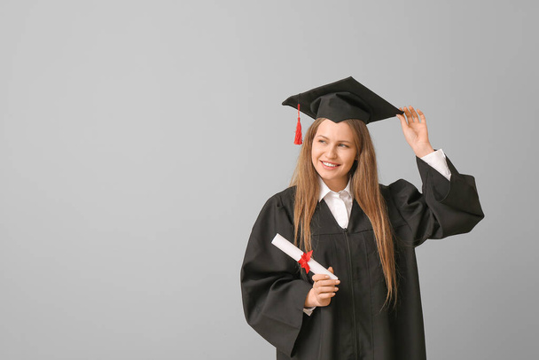 Female graduating student with diploma on light background - Foto, imagen