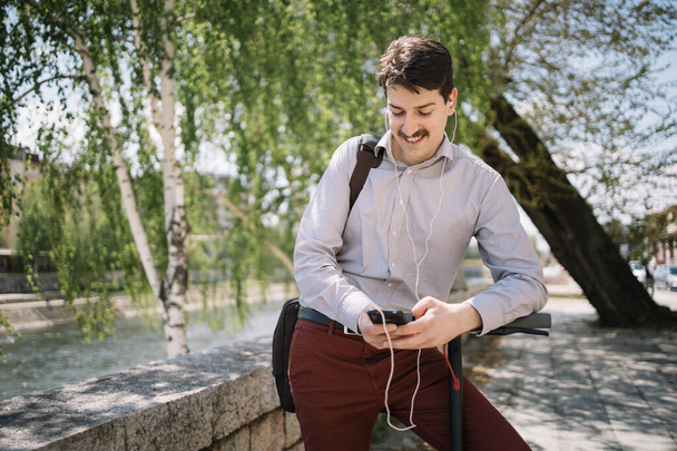 Businessman with headphones standing on riverside and using phone - Φωτογραφία, εικόνα