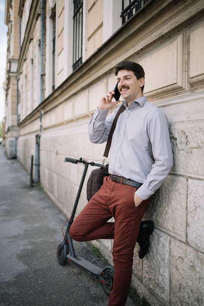 Sonriente hombre con bigote hablando por teléfono mientras se apoya en la pared
 - Foto, Imagen