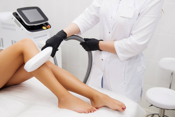 Laser epilation and cosmetology in beauty salon. Hair removal procedure. Laser epilation, cosmetology, spa, and hair removal concept. Beautiful brunette woman getting hair removing on legs - Photo, Image