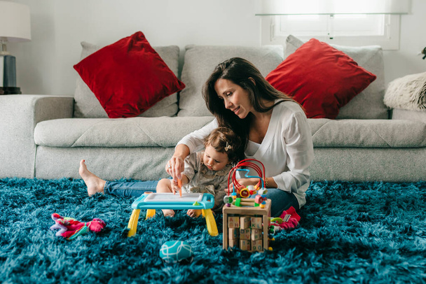junge hübsche Mutter spielt mit ihrer Tochter auf dem Fußboden im heimischen Wohnzimmer - Foto, Bild