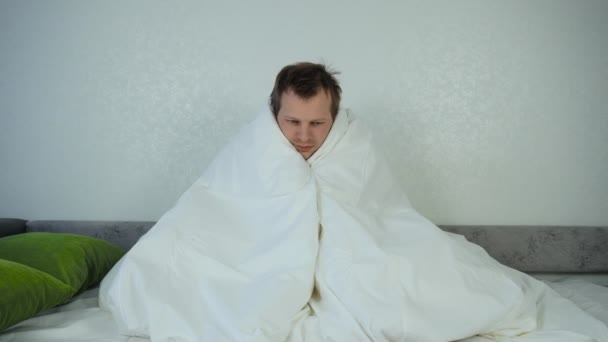 An unbalanced sick man wrapped himself in a blanket and sits on a sofa. Mental disorder and depression concept, cold temperature - Séquence, vidéo