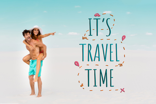 smiling young man piggybacking girlfriend while woman pointing with finger away on sandy beach, it is travel time illustration - Photo, Image