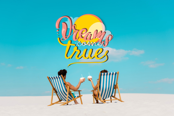 back view of young couple sitting in deck chairs with coconut drinks on sandy beach, dreams come true illustration - Photo, Image