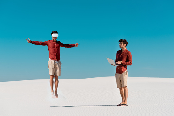 collage of young man jumping in vr headset and with laptop on sandy beach - Photo, Image