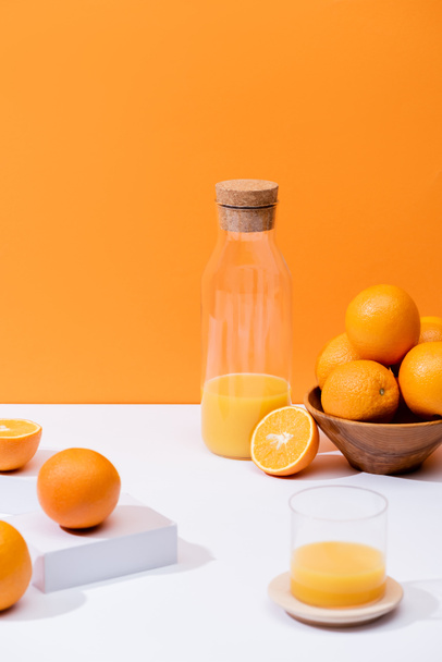 fresh orange juice in glass and bottle near oranges in bowl on white surface isolated on orange - Photo, image