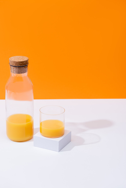 fresh orange juice in glass and bottle on white surface isolated on orange - Фото, изображение