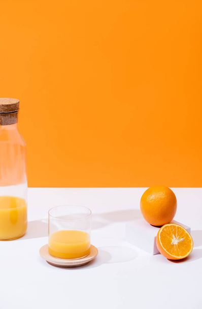 frischer Orangensaft in Glas und Flasche in der Nähe von Orangen auf weißer Oberfläche isoliert auf Orange - Foto, Bild