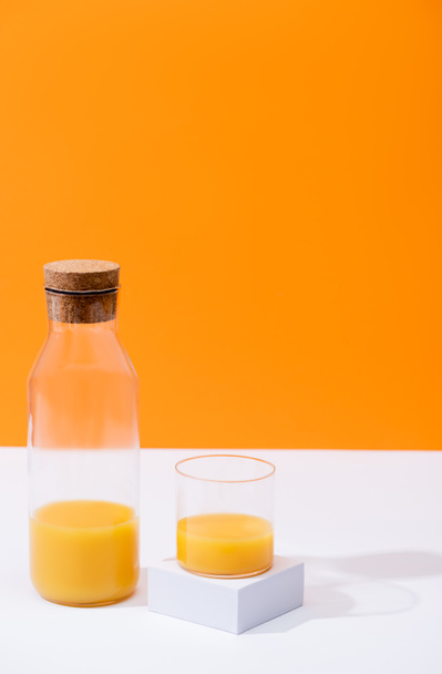 zumo de naranja fresco en vaso y botella sobre superficie blanca aislada sobre naranja
 - Foto, Imagen