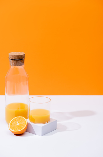 fresh orange juice in glass and bottle near cut fruit on white surface isolated on orange - 写真・画像