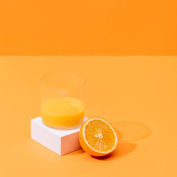 オレンジに分離されたオレンジと白のキューブの半分近くのガラスの中の新鮮なオレンジジュース - 写真・画像