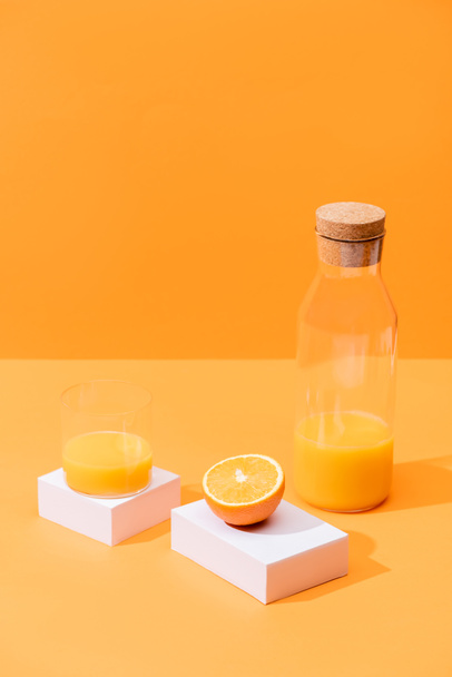 fresh orange juice in glass and bottle near cut orange and white cubes isolated on orange - 写真・画像