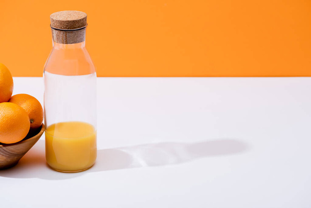 zumo de naranja fresco en botella de vidrio cerca de naranjas en cuenco de madera en superficie blanca aislado en naranja
 - Foto, Imagen