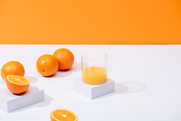 φρέσκος χυμός πορτοκαλιού σε ποτήρι κοντά σε ώριμα πορτοκάλια σε λευκή επιφάνεια που απομονώνεται σε πορτοκάλι - Φωτογραφία, εικόνα
