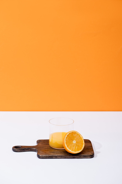 zumo de naranja fresco en vidrio cerca de fruta cortada en tabla de cortar de madera en la superficie blanca aislada en naranja
 - Foto, Imagen