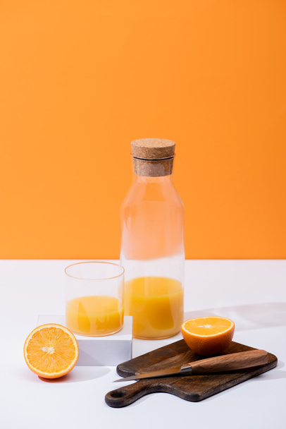 friss narancslé üvegben és üvegben, vágott gyümölcs közelében fa vágódeszkán, késsel fehér felületen, narancssárgán izolálva - Fotó, kép