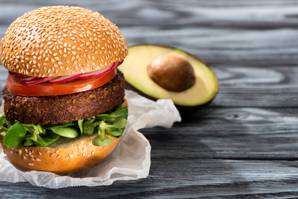 selective focus of tasty vegan burger with radish served on wooden table with avocado half - Foto, imagen