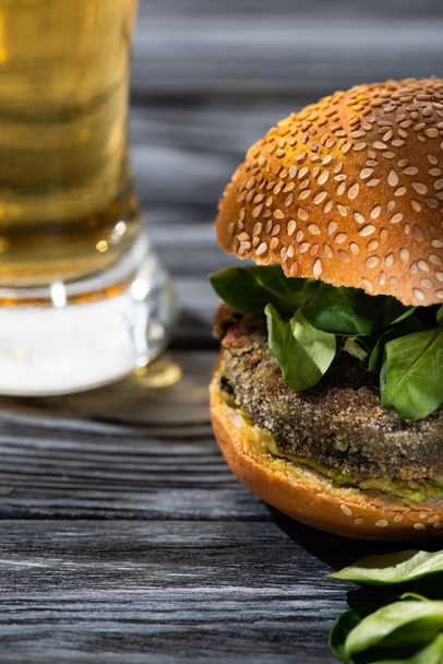 selective focus of tasty vegan burger with microgreens served on wooden table with glass of beer - Foto, Imagem