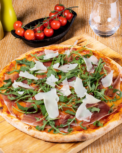 Fresh oven baked traditional prosciutto, rucola, tomato and parmesan pizza, served on a wooden board - Photo, image