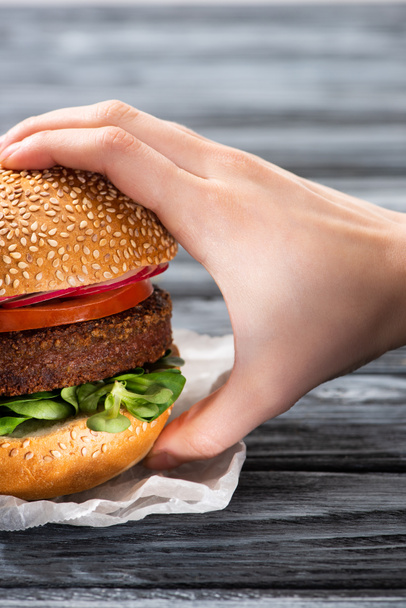 przycięty widok kobiecej ręki ze smacznym wegańskim burgerem na drewnianym stole - Zdjęcie, obraz
