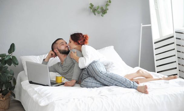 Мужчина и женщина общаются на ноутбуке. Счастливая семья по утрам в постели дома
.  - Фото, изображение