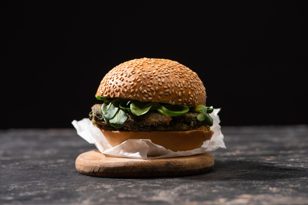 tasty vegan burger with microgreens served on wooden board isolated on black - Fotó, kép