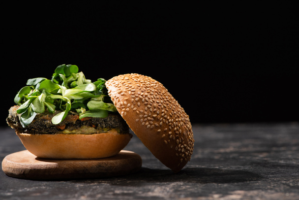 tasty vegan burger with microgreens served on wooden board isolated on black - Foto, Bild