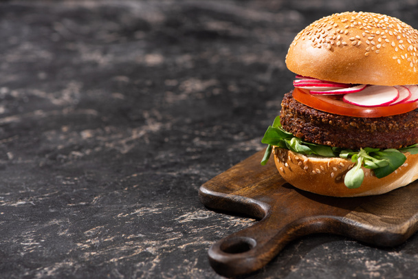 tasty vegan burger with vegetables served on wooden cutting board on textured surface - 写真・画像