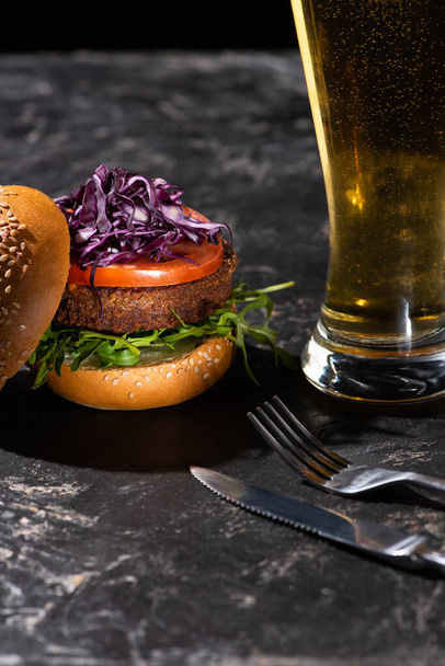 tasty vegan burger with tomato, red cabbage and greens served on textured surface with beer and cutlery - Photo, Image