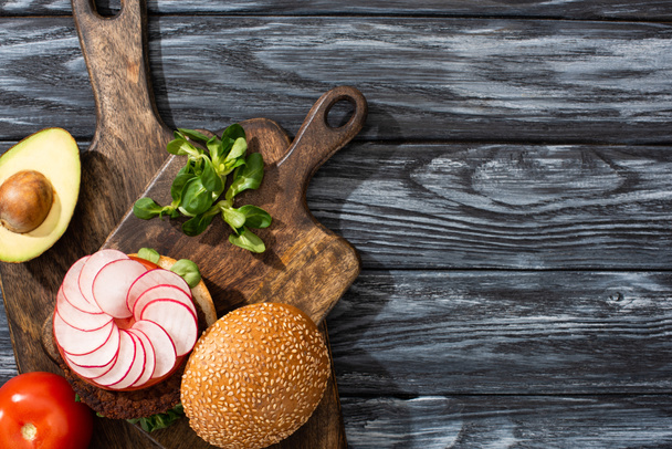 top view of tasty vegan burger with microgreens, radish, tomato and avocado on cutting boards served on wooden table - Fotografie, Obrázek