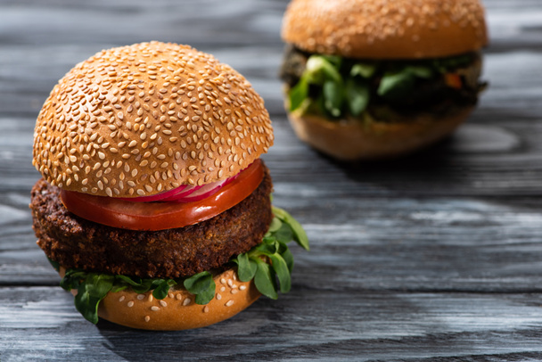 selective focus of tasty vegan burgers with vegetables served on wooden table - Фото, изображение