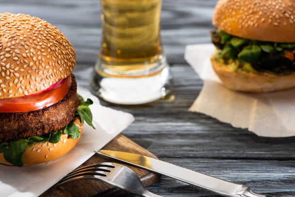 selective focus of tasty vegan burgers served on wooden table with beer and cutlery - Foto, immagini