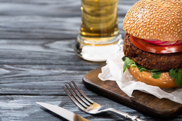 selective focus of tasty vegan burger served on wooden table with beer and cutlery - 写真・画像