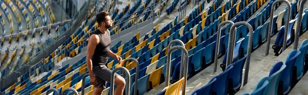 young sportsman walking on stairs among seats at stadium, panoramic shot - Photo, image