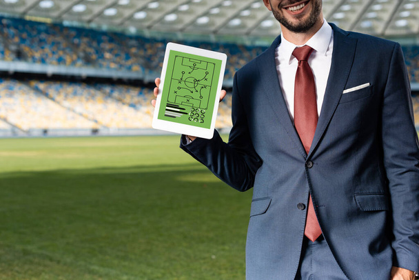 vue recadrée d'un jeune homme d'affaires souriant en costume tenant une tablette numérique avec formation à l'écran au stade
 - Photo, image