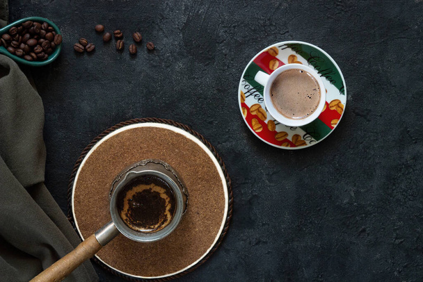 Кавоварка з свіжою кавою і чашка капучино на дерев'яному підставці на темному тлі з кавовими бобами і зеленою бавовняною тканиною. - Фото, зображення