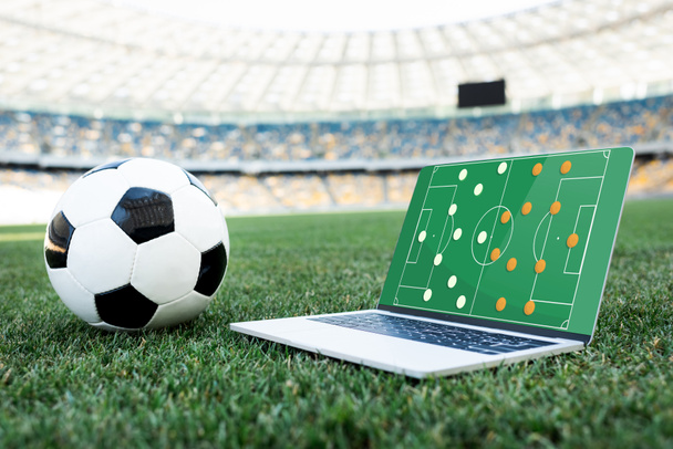futball labda és laptop alakzat a képernyőn füves focipályán a stadionban - Fotó, kép