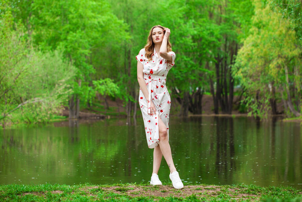 Full body portrait of a young beautiful woman in white dress posing by the lake - Foto, Imagen