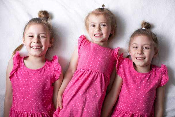 ピンクのドレスを着た3人の女の子がベッドの上に横になって笑っている - 写真・画像
