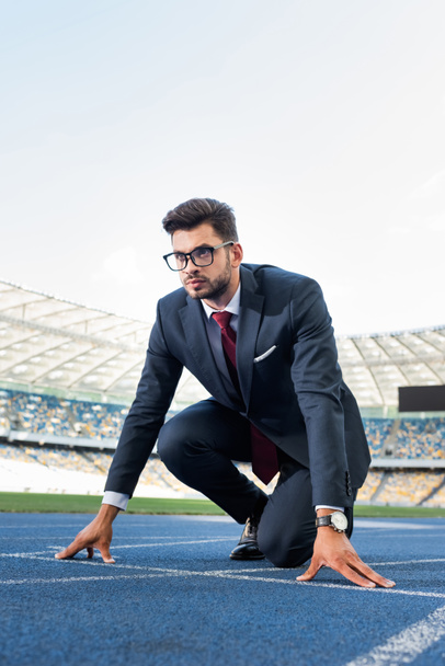 νεαρός επιχειρηματίας με κοστούμι στη θέση εκκίνησης για πίστα στο γήπεδο - Φωτογραφία, εικόνα