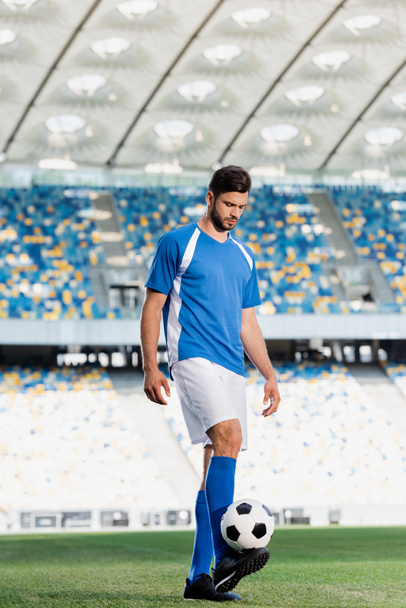 profesionální fotbalista v modré a bílé uniformě s míčem na fotbalovém hřišti na stadionu - Fotografie, Obrázek