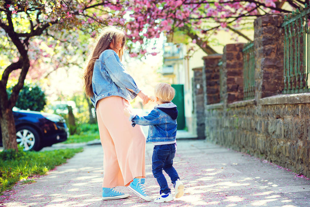 Šťastná matka a syn kráčejí po jarní ulici. Roztomilý chlapec a maminka baví spolu venku. Šťastný Den matek. Rodina, móda a dovolená. Hravé dítě a mladá matka si užívají jaro. - Fotografie, Obrázek