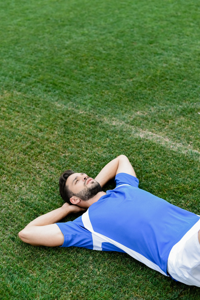 profesionální fotbalista v modré a bílé uniformě leží na fotbalovém hřišti na stadionu - Fotografie, Obrázek