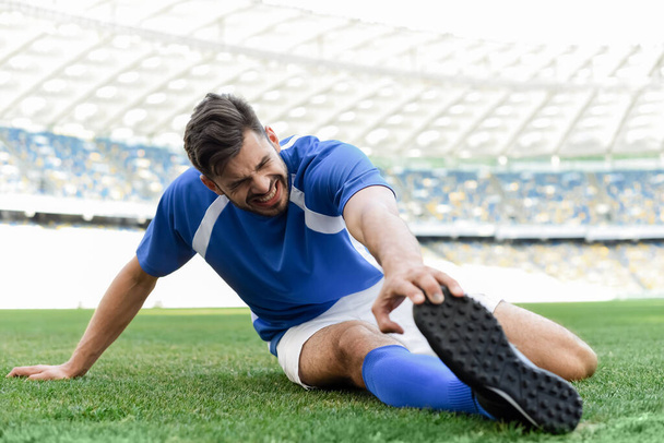 professional soccer player in blue and white uniform stretching on football pitch at stadium - Фото, изображение
